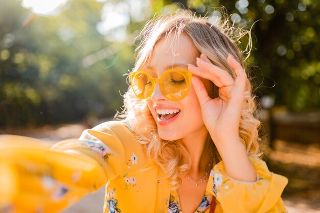 Porträt der schönen blonden stilvollen lächelnden Frau in der gelben Bluse, die Sonnenbrille trägt, die selfie Foto macht