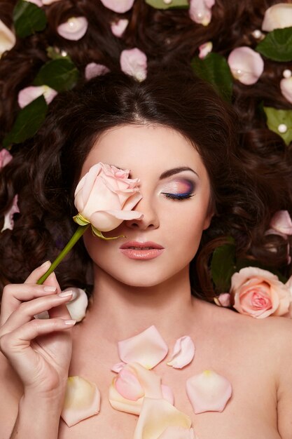 Porträt der schönen Brunettefrau mit dem langen gelockten Haar und hellem Make-up mit Blumen im Haar