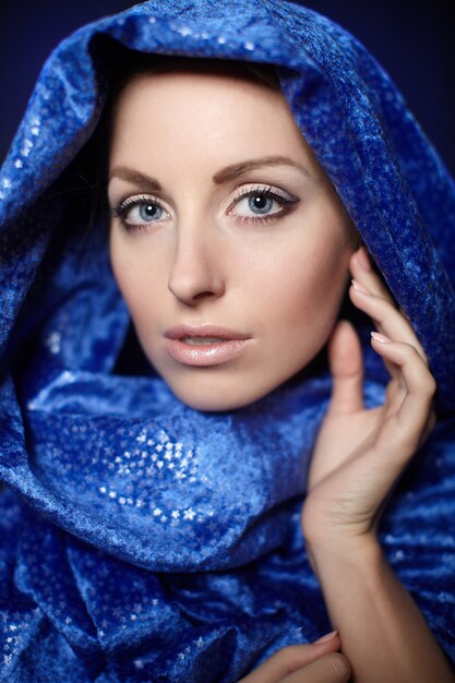 Porträt der schönen Frau mit Abendmake-up. Modell, das im Studio mit blauem Textil auf ihrem Kopf aufwirft