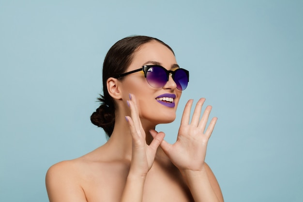 Porträt der schönen Frau mit hellem Make-up und Sonnenbrille auf blauem Studio