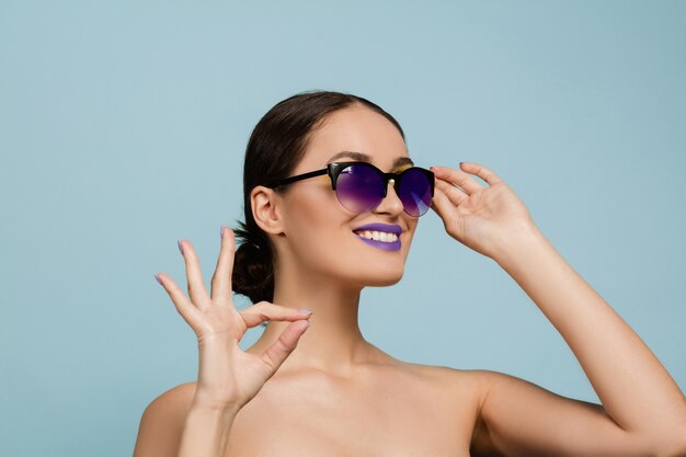 Porträt der schönen Frau mit hellem Make-up und Sonnenbrille. Stilvolle, modische Marke und Frisur. Farben des Sommers. Zeigt Anzeichen von nett.