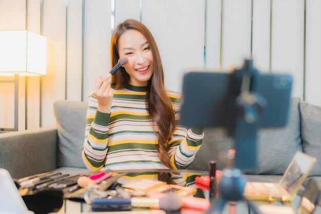 Porträt der schönen jungen asiatischen Frau Bewertungen und verwendet Kosmetik auf dem Sofa