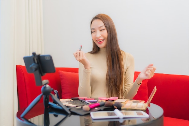 Porträt der schönen jungen asiatischen Frau Bewertungen und verwendet Kosmetik auf dem Sofa