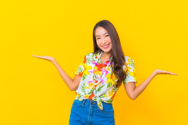 Porträt der schönen jungen asiatischen Frau, die buntes Hemd auf gelber Wand trägt