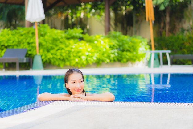 Porträt der schönen jungen asiatischen Frau, die sich um den Außenpool im Hotelresort entspannt