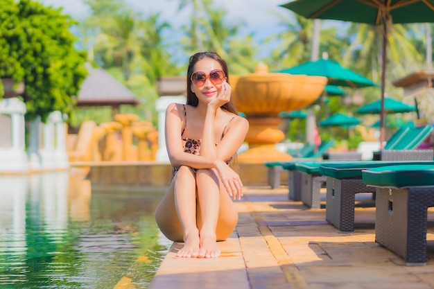 Porträt der schönen jungen asiatischen Frau, die sich um den Außenpool im Hotelresort entspannt