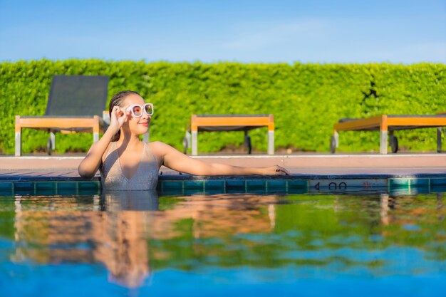 Porträt der schönen jungen asiatischen Frau, die sich um den Außenpool im Hotelresort entspannt