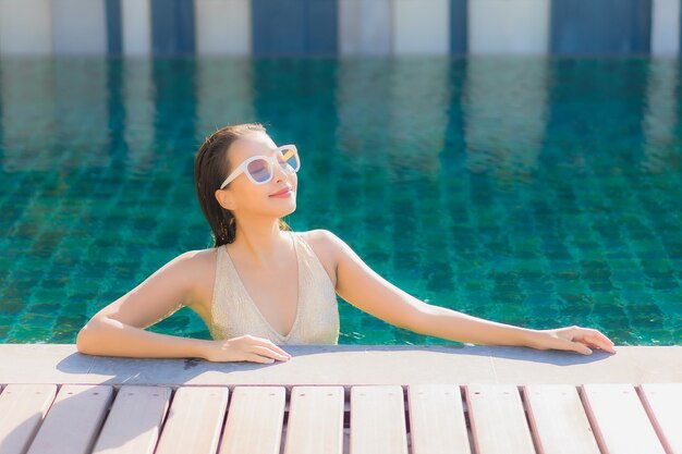 Porträt der schönen jungen asiatischen Frau, die sich um den Außenpool im Hotelresort entspannt