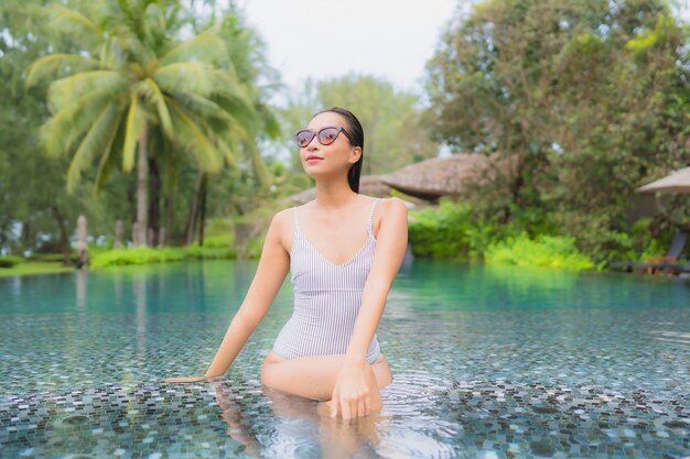 Porträt der schönen jungen asiatischen Frau, die sich um den Außenpool im Hotelresort fast Meer entspannt