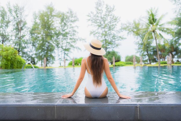 Porträt der schönen jungen asiatischen Frau, die sich um den Außenpool im Hotelresort fast Meer entspannt