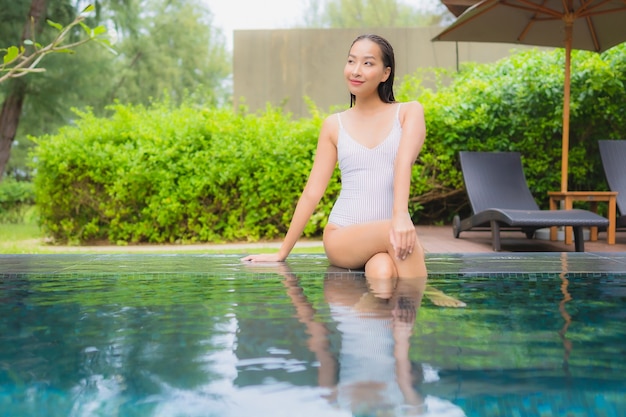 Porträt der schönen jungen asiatischen Frau, die sich um den Außenpool im Hotelresort fast Meer entspannt