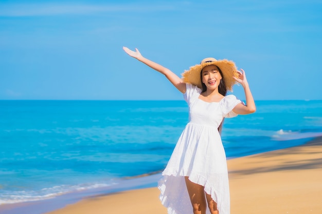 Porträt der schönen jungen asiatischen Frau, die um Strand mit weißen Wolken auf blauem Himmel im Reiseurlaub entspannt