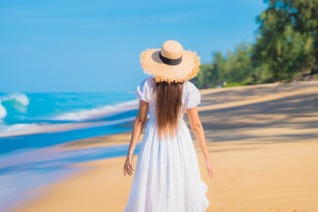 Porträt der schönen jungen asiatischen Frau, die um Strand mit weißen Wolken auf blauem Himmel im Reiseurlaub entspannt