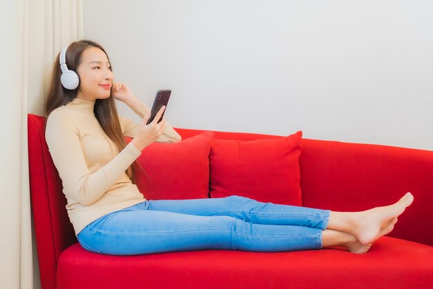 Porträt der schönen jungen asiatischen Frau hört Musik auf Sofa im Wohnzimmer Interieur