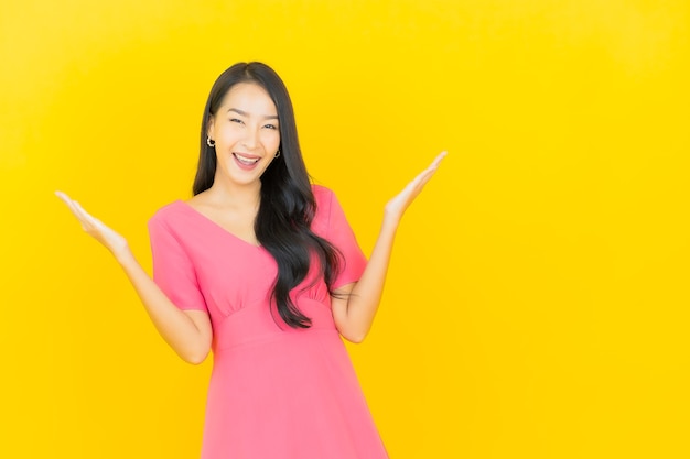 Porträt der schönen jungen asiatischen Frau lächelt im rosa Kleid auf gelber Wand