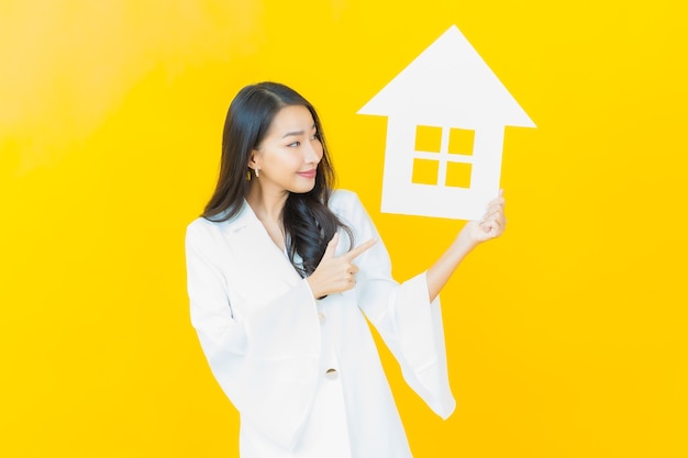 Porträt der schönen jungen asiatischen frau mit papierhaus auf gelber wand
