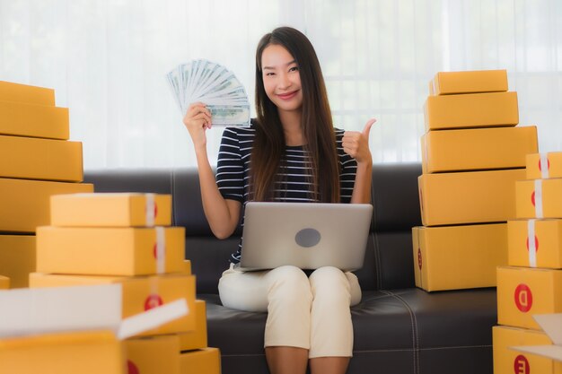 Porträt der schönen jungen asiatischen Frau mit Papppaketboxen und Geld