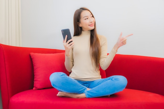 Porträt der schönen jungen asiatischen Frau verwendet Smartphone auf Sofa im Wohnzimmer Interieur