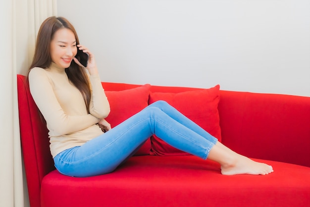 Porträt der schönen jungen asiatischen Frau verwendet Smartphone auf Sofa im Wohnzimmer Interieur