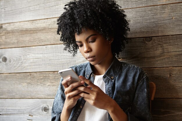 Porträt der schönen jungen dunkelhäutigen Frau mit Afro-Haarschnitt, der stilvolles Jeanshemd trägt