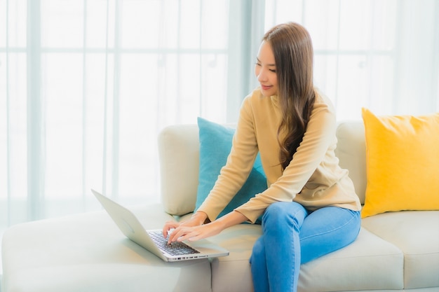 Porträt der schönen jungen Frau, die Laptop auf Sofa im Wohnzimmer verwendet