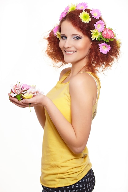 Porträt der schönen lächelnden rothaarigen Ingwerfrau im gelben Stoff mit gelben rosa bunten Blumen im Haar lokalisiert auf weißen Halteblumen