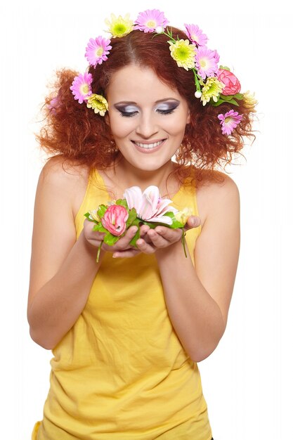 Porträt der schönen lächelnden rothaarigen Ingwerfrau im gelben Stoff mit gelben rosa bunten Blumen im Haar lokalisiert auf weißen Halteblumen