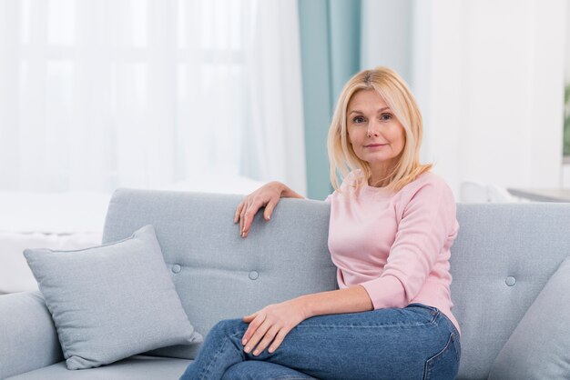 Porträt der schönen reifen Frau, die auf der Couch sitzt