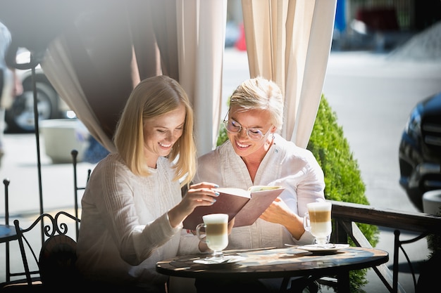 Porträt der schönen reifen Mutter und ihrer Tochter, die Tasse hält, die zu Hause sitzt