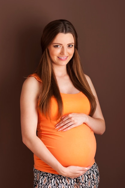 Kostenloses Foto porträt der schönen schwangeren frau auf brauner wand