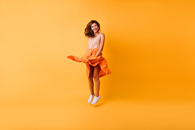 Porträt der stilvollen Dame von debonair, die im Studio springt. Wunderschönes Ingwermädchen im orangefarbenen Rock, der Spaß hat.