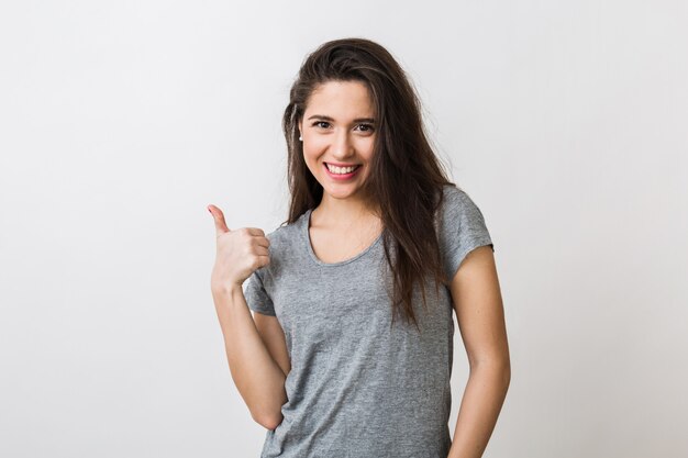 Porträt der stilvollen jungen hübschen Frau, die im grauen T-Shirt auf lächelt, lokalisiert, zeigt Daumen hoch, glückliche, positive Geste
