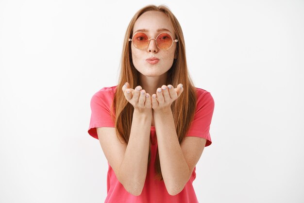 Porträt der stilvollen sorglosen und selbstbewussten weiblichen Frau in der rosa runden Sonnenbrille, die warmen liebevollen Kuss bläst