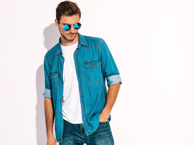 Porträt der tragenden Jeanskleidung und -sonnenbrille des hübschen lächelnden stilvollen Modells des jungen Mannes. Mode Mann