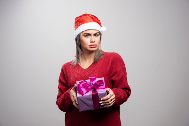 Porträt der traurigen Frau, die mit Feiertagsgeschenk auf grauem Hintergrund aufwirft.