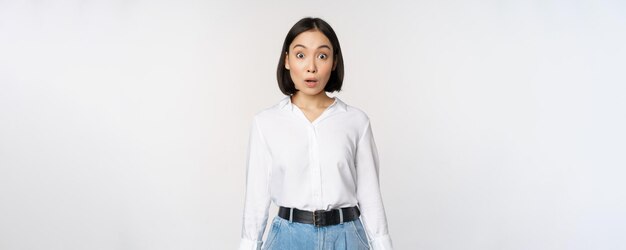 Porträt der überraschten asiatischen Geschäftsfrau der jungen Bürofrau, die erstaunt nach Luft schnappt und sagt, wow steht, beeindruckt von Nachrichten vor weißem Hintergrund