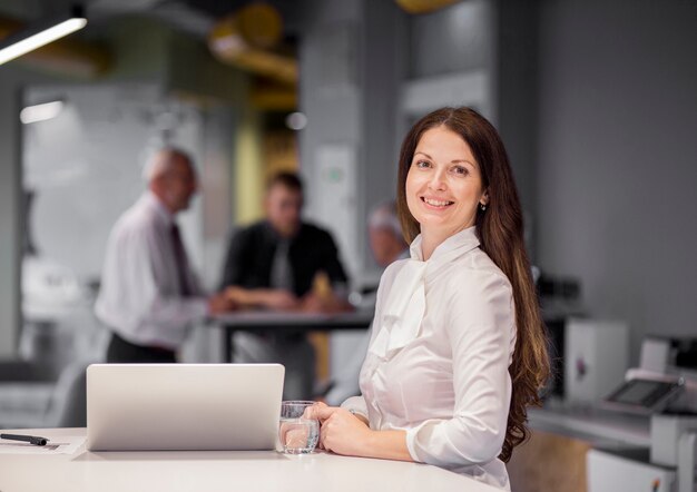 Porträt der überzeugten Geschäftsfrau mit Laptop und Glas Wasser am Arbeitsplatz