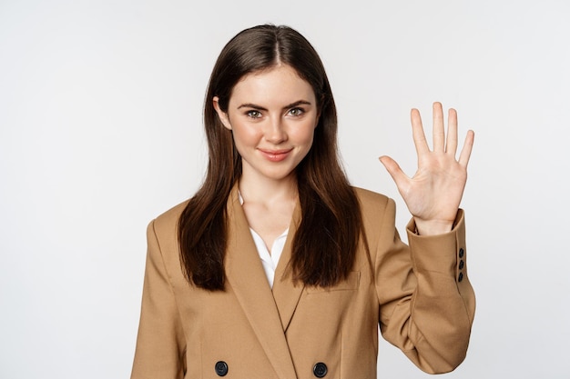 Porträt der Unternehmensfrau, Verkäuferin, die Finger der Nummer fünf zeigt und lächelt und im Anzug auf weißem Hintergrund steht