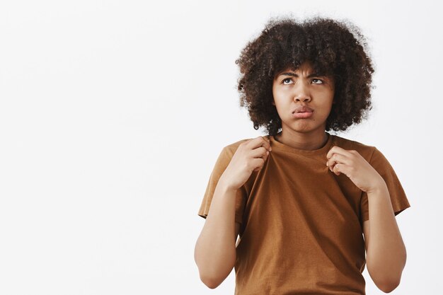 Porträt der unzufriedenen düsteren und belästigten niedlichen afroamerikanischen Frau im braunen T-Shirt, das ausatmet und mit Abneigung gegen Wetter auf Sonne schaut