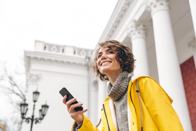 Porträt der zufriedenen Frau 20s, die modernes Gerät hält, empfangen Textnachricht auf ihrem Smartphone beim Sein im Freien