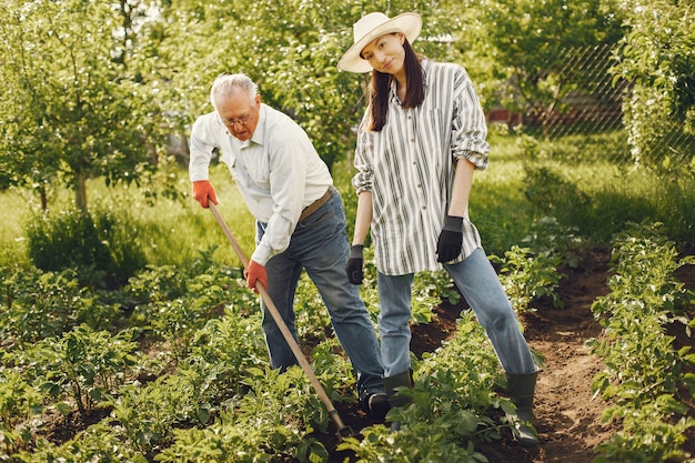 Porträt des älteren Mannes in einem Hut, der mit Enkelin im Garten arbeitet