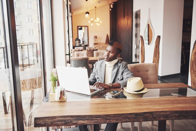 Porträt des Afroamerikanermanns, der an einem Café sitzt und an einem Laptop arbeitet