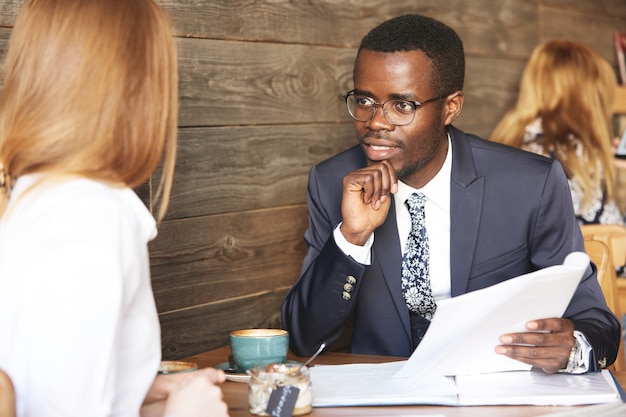 Porträt des afroamerikanischen Rekrutierers in der Abendgarderobe, die rothaarige Bewerberin interviewt