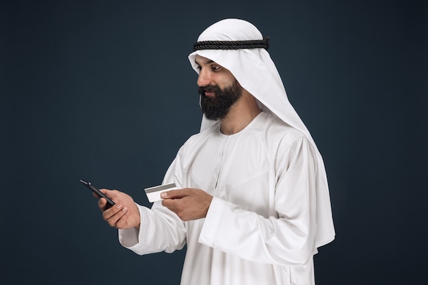 Porträt des arabischen Saudi-Scheichs. Mann mit Smartphone zum Bezahlen von Rechnungen, Online-Shopping oder Wetten.