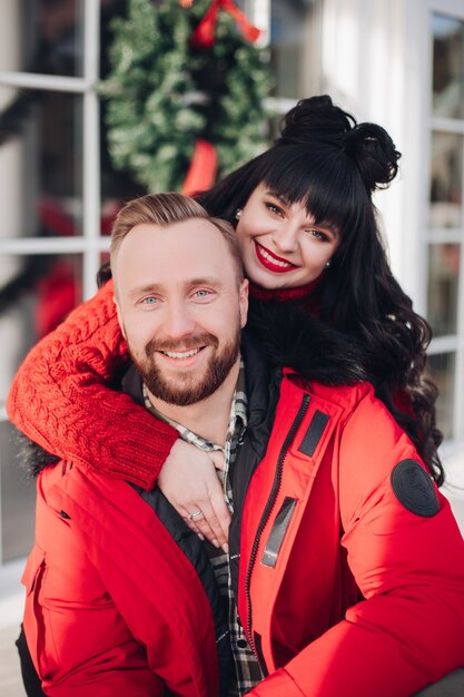 Porträt des attraktiven kaukasischen Paares im roten Lächeln an der Kamera. Verschwommener Weihnachtskranz im Hintergrund.
