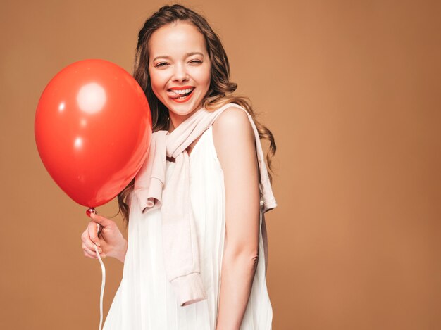 Porträt des aufgeregten jungen Mädchens, das im weißen Kleid des modischen Sommers aufwirft. Lächelnde Frau mit der roten Ballonaufstellung. Modell bereit für die Party