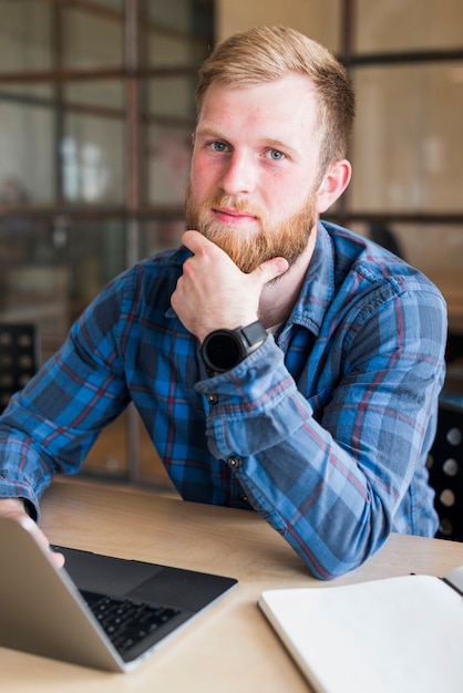 Kostenloses Foto porträt des bärtigen mannes sitzend vor laptop am arbeitsplatz