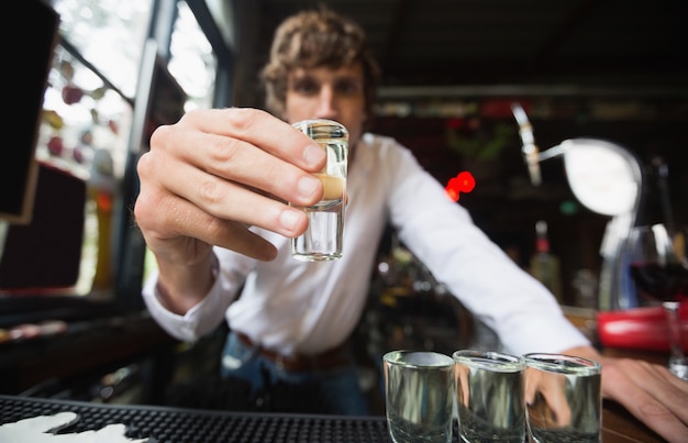 Kostenloses Foto porträt des barkeepers, der tequila-schnapsglas am bartheke hält