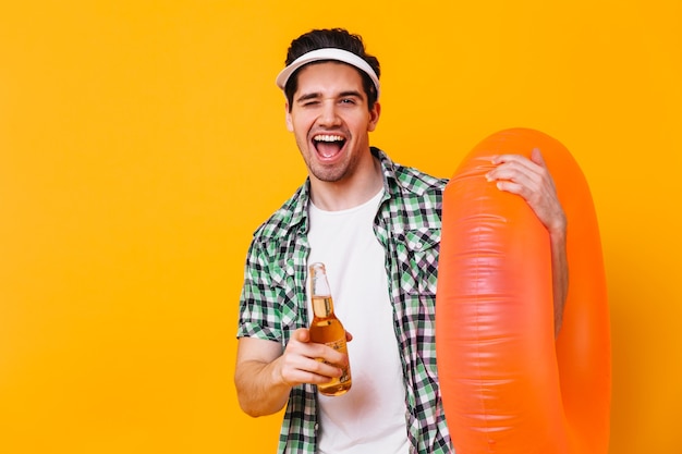 Porträt des Brunet-Kerls in der weißen Kappe, die zur Kamera zeigt. Mann mit Gummiring, der Bier hält.