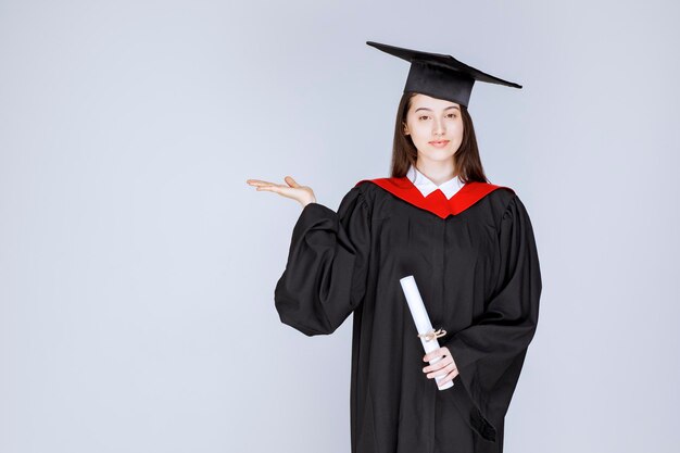 Porträt des Doktoranden im Kleid, das Diplom hält und steht. Foto in hoher Qualität